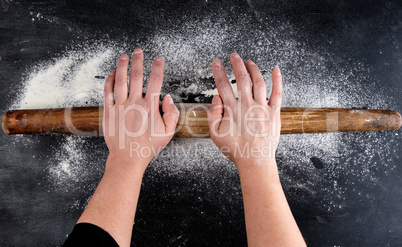 Brown wooden rolling pin in female hands on a black background w