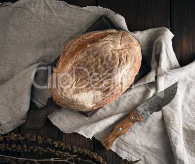 baked oval bread made from rye flour on a wooden cutting board