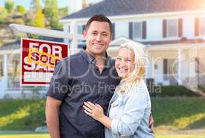 Happy Couple In Front of Sold Real Estate Sign and Beautiful House