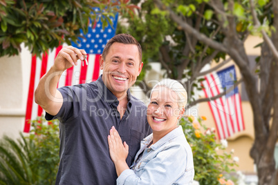 Happy Couple With New House Keys In Front of House with Flags