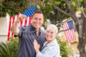 Happy Couple With New House Keys In Front of House with Flags