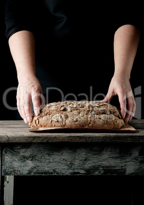 female hands hold oval baked rye bread with pumpkin seeds