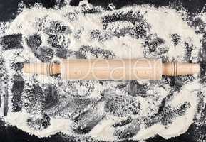 wooden rolling pin and white wheat flour scattered on a black ba