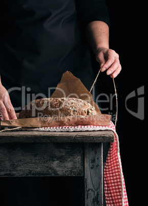 girl in black clothes wraps a whole baked loaf of bread in brown