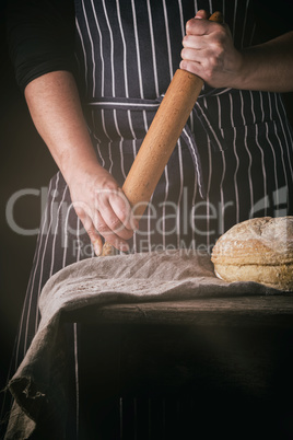woman in an apron holds a wooden rolling pin next to baked round