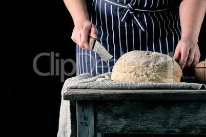 woman in an apron with a knife in her hand about to cut round ba