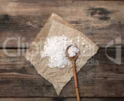 large white salt on a brown piece of paper and a wooden spoon
