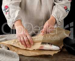 female hands are wrapped in brown paper whole fresh sea bass fis