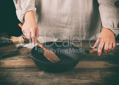 women's hands hold a round black pan and a wooden spatula