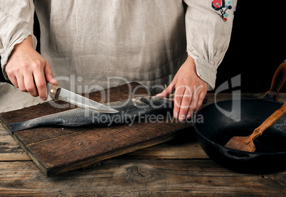 woman in gray linen clothes cleans the fish sea bass scales