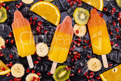 Fruit ice cream on stick with slices fruits on black slate