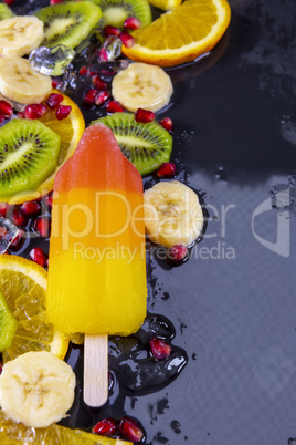 Fruit ice cream on stick with slices fruits on black slate