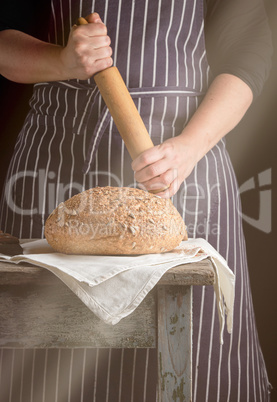 woman in an apron holds a wooden rolling pin next to baked round