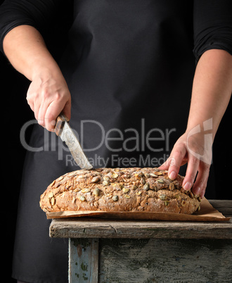 female hands hold oval baked rye bread with pumpkin seeds