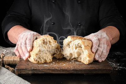 baker in black uniform broke in half a whole baked loaf of whit