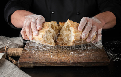 baker in black uniform broke in half a whole baked loaf