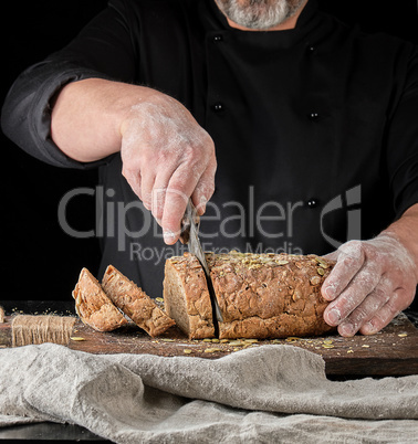 baker cuts a knife into slices of rye bread with pumpkin seeds