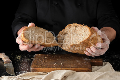 chef in a black uniform holds broken in half round rye bread