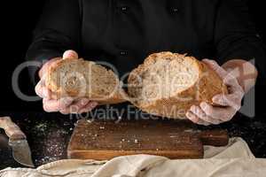 chef in a black uniform holds broken in half round rye bread