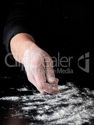chef in black uniform sifts through his fingers white wheat flou