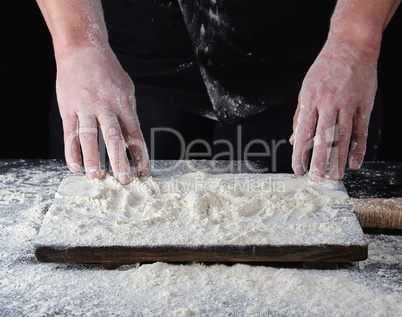 cook in a black uniform put two hands on a table sprinkled with