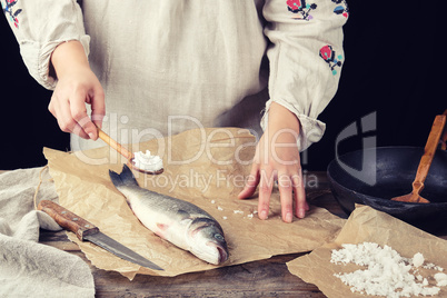 girl in a gray long linen dress holds a full spoonful of salt