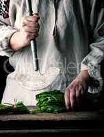 woman in a gray linen dress is cutting green leaves of fresh sor