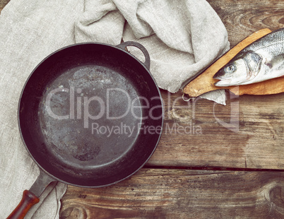 fresh whole sea bass fish on a brown board, next to it is an emp