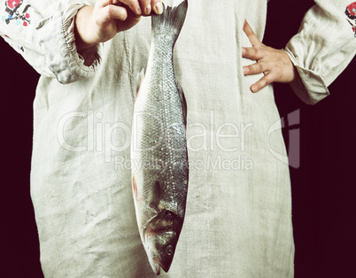 woman in gray linen clothes holding a fresh sea bass fish