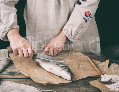 woman in gray linen clothes cleans the fish sea bass scales on a