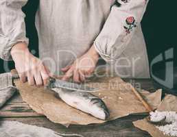 woman in gray linen clothes cleans the fish sea bass scales on a