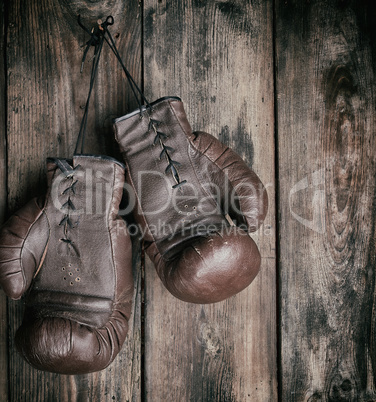 very old leather brown boxing gloves hang on an old shabby woode
