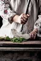 woman in a gray linen dress is cutting green leaves of fresh sor