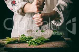 woman in a gray linen dress is cutting green leaves of fresh sor