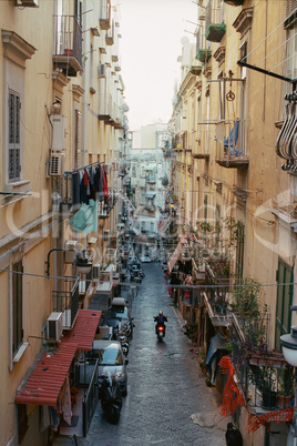 Alleyway with motorbike driving among old houses in Naples, Italy