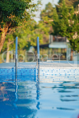 An open swimming pool with a shiny railing and a sunny background