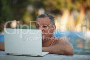 A middle aged man in the swimming pool watching something on a laptop