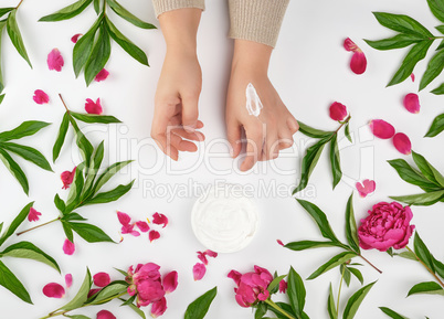 two female hands and a jar with thick cream and burgundy floweri