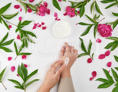two female hands and a jar with thick cream and burgundy floweri