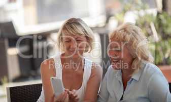 Two middle aged women sitting outside and smiling while looking at a smartphone screen