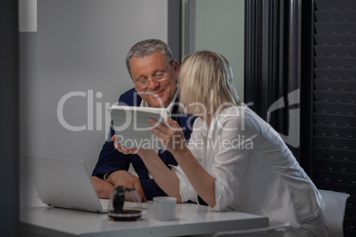 A middle aged couple at the table with their devices