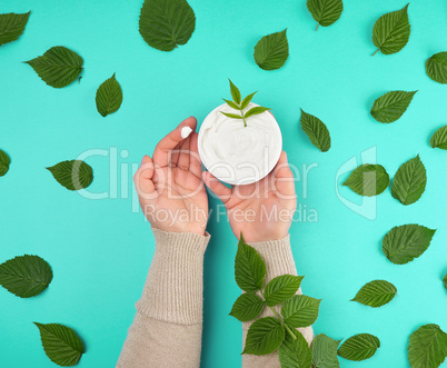hands of a young girl with smooth skin holding a round jar of cr