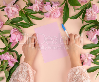 female hand holds hand a white pen over empty pink sheet of pape