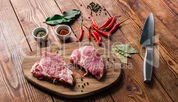 Two raw steak with spices and knife on wooden table.