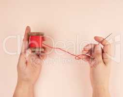 two hands hold a wooden bobbin with red wool threads