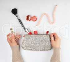 two female hands and a silver cosmetic bag with cosmetics