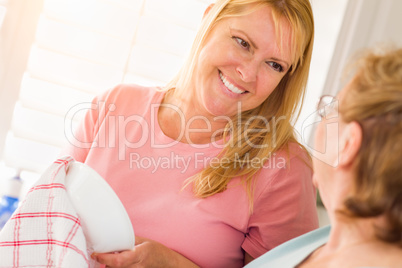 Senior Adult Woman and Young Daughter Talking At Sink in Kitchen