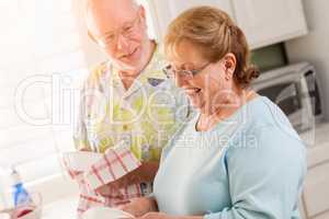 Senior Adult Couple Having Fun Washing Dishes Together In Kitchen