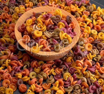 multicolored spiral raw pasta fusilli in a wooden bowl