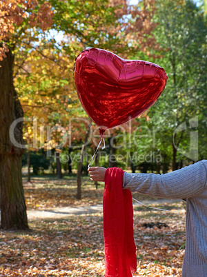 female hand holding a red balloon in the shape of a heart